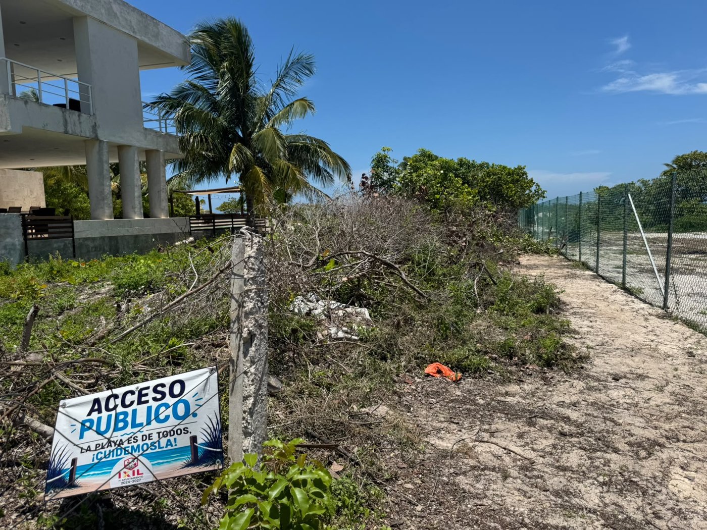 Señal del Ayuntamiento de Ixil que indica acceso público a la playa junto a un predio cercado.