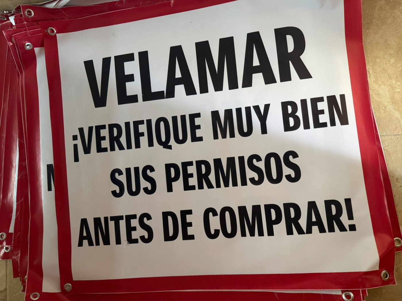 Lona informativa con la leyenda “Velamar: verifique muy bien sus permisos antes de comprar”.